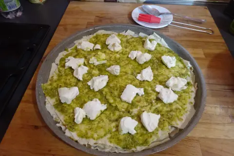 Une pizza à la pâte fine, recouverte de sauce verte et de morceaux de fromage blanc. Un délice inspiré du pain sarde.