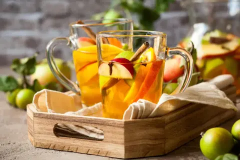 Zwei Gläser mit warmem Apfel-Zimt-Wasser, garniert mit Apfelstücken und Zimtstangen, stehen auf einem Holzteller.
