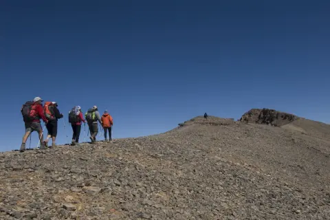 Randonneurs sur le flanc rocailleux du mont M'goun, sous un ciel bleu intense.