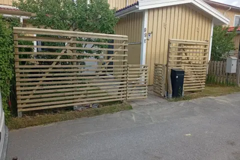 Nya trästaket byggs för att bygga insynsskydd vid ett gult hus.