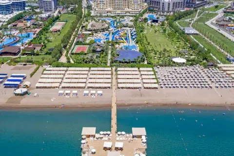 Widok z lotu ptaka na rozległy royal holiday palace z basenami, zjeżdżalniami, kortami tenisowymi i plażą z leżakami.