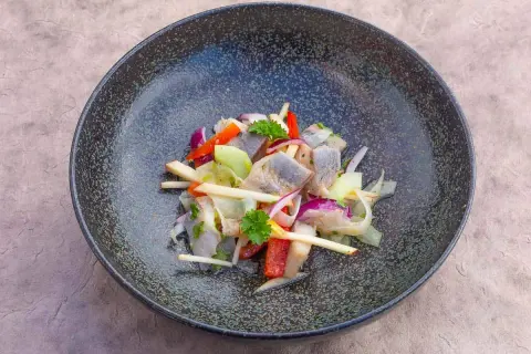 Heringssalat Hausfrauenart: ein deftiger Salat mit Hering, Apfel, Zwiebeln und Paprika in einer dunklen Schüssel.