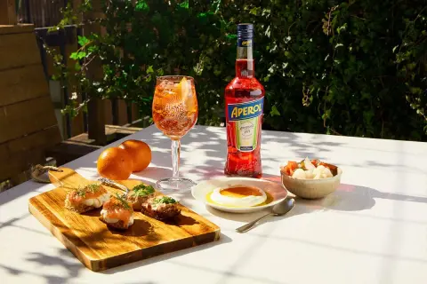 En Aperol Spritz med tilltugg till aperol spritz: laxsnittar, ost med honung och inlagda grönsaker.