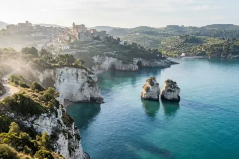 Panoramica mozzafiato del Gargano, Puglia, con scogliere bianche, mare cristallino, faraglioni e un borgo arroccato.