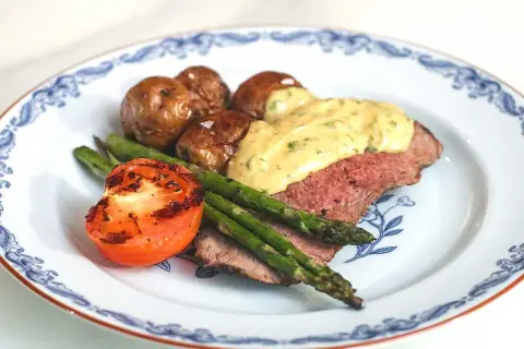 En tallrik med ryggbiff, potatis, sparris och tomat. En krämig sås toppar köttet. Ett perfekt ryggbiff recept!
