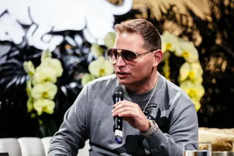Scott Storch, known for his hit songs, speaks into a microphone, wearing sunglasses and a grey sweatshirt.