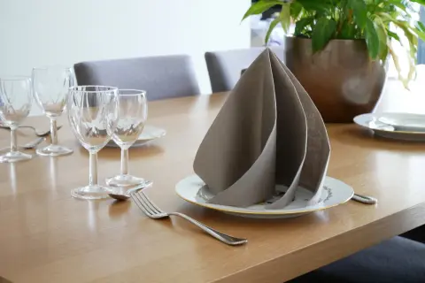 Un pliage serviette papier 2 couleurs, élégant, sur une table dressée avec des verres et des couverts.
