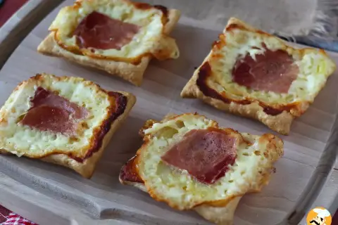 Cztery kwadratowe tartaletki z ciasta francuskiego, wypełnione roztopionym serem i plastrami szynki. Idealne na szybką przekąskę w stylu raclette.