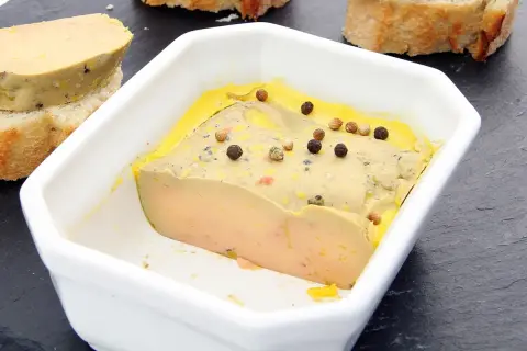 Un foie gras mi-cuit, à la texture parfaite, est servi dans un plat blanc, parsemé de grains de poivre. La température idéale pour savourer ce délice.