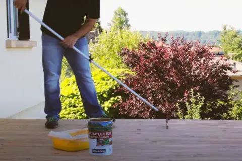 Application d'un saturateur sur une terrasse en bois. Le rouleau est en action pour un nettoyage et une protection parfaits.