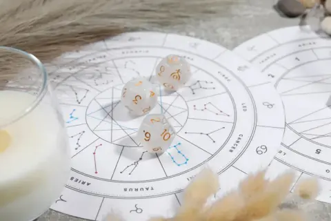 Karty zodiaku, kostki z symbolami planet i płonąca świeca tworzą mistyczną atmosferę.