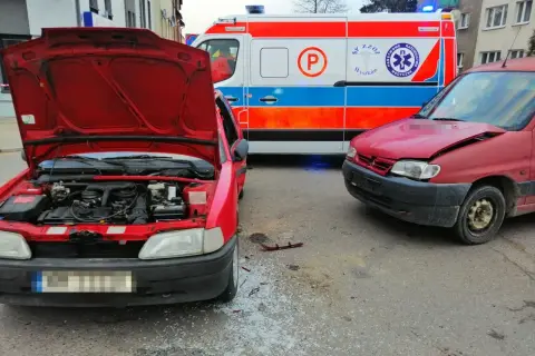 Wypadek po wymuszeniu pierwszeństwa. Dwa czerwone samochody po kolizji, obok karetka pogotowia.