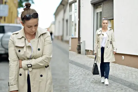 Kobieta w beżowym trenczu i sportowych stylizacjach, z torebką i okularami przeciwsłonecznymi, idzie po brukowanej ulicy.
