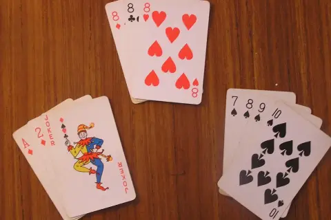 Na stole leżą karty: joker, dwójka i as, a także cztery ósemki i sekwencja pikowa od 7 do 10.