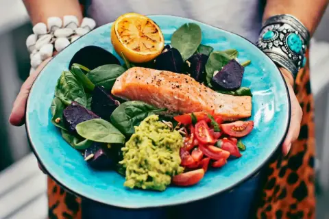 En matig sallad med lax, avokado, rödbetor, tomater och citron på en turkos tallrik.