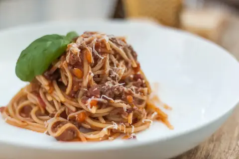 Pyszne spaghetti bolognese z parmezanem i listkiem bazylii na białym talerzu.