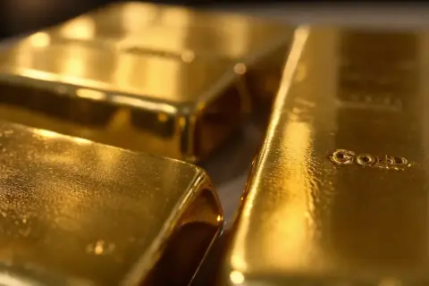 Trzy błyszczące sztabki złota, jedna z napisem "GOLD".
