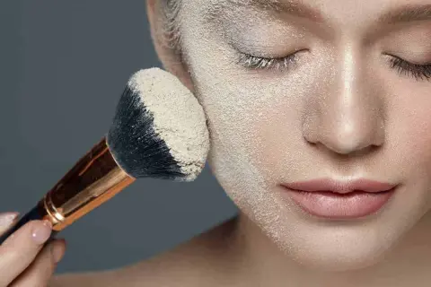 Un pennello applica cipria su un viso, mostrando la tecnica del "baking" per un trucco impeccabile.