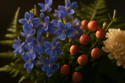 En bukett med små, blå lobelia-blommor, röda bär och en krämvit blomma.