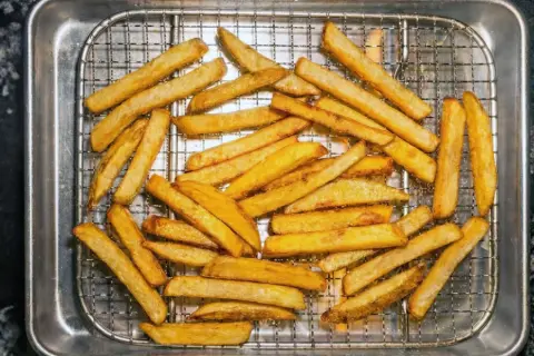 En hög med gyllene, krispiga pommes frites ligger på ett galler i en plåt. Perfekt för en snabb aptitretare.