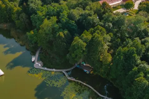 Malownicze pojezierze lubuskie z żaglówką na wodzie, drewnianym pomostem i bujną zielenią drzew.
