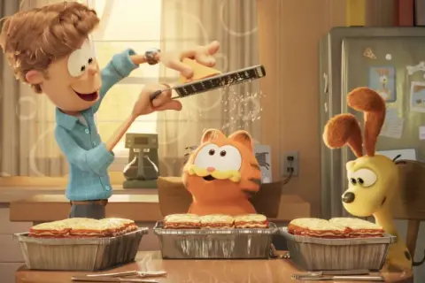 Jon reibt Käse für Lasagne, während Garfield und Odie gespannt zuschauen. Ein Festmahl für garfield – eine extra portion abenteuer!