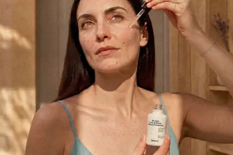 Kobieta aplikuje serum z niacynamidem i witaminą C na skórę. Produkt w białej buteleczce z pipetą.