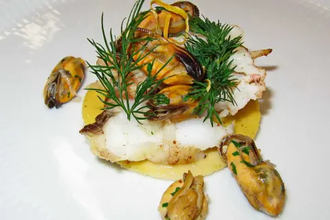 Délicieux plat de joue de lotte poêlée, garni de moules et d'aneth frais, servi sur un lit de purée.