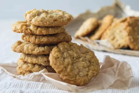 Ein Stapel goldbrauner Haferflocken-Bananen-Cookies auf einem weißen Tuch, daneben weitere Kekse.
