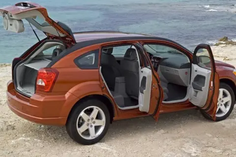 Orange Dodge Caliber 2007 med öppna dörrar och baklucka vid havet. Perfekt för en roadtrip!