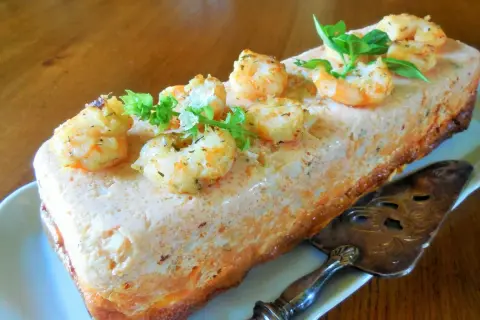 Un délicieux pain de poisson aux crevettes et herbes fraîches, prêt à être découpé avec une pelle à tarte ornée.