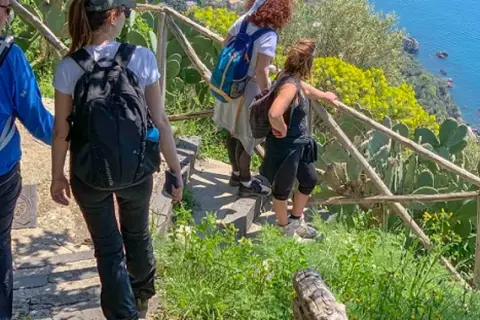 Gruppo di escursionisti sul sentiero degli dei ad Agerola, con vista sul mare blu e vegetazione mediterranea.