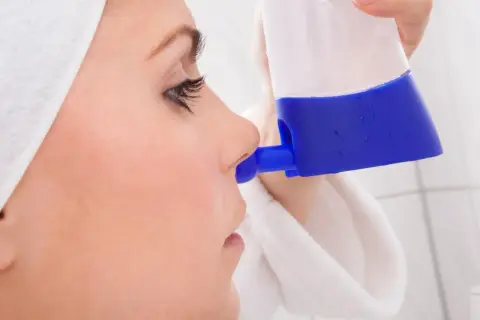 Kobieta w białym ręczniku płucze zatoki irygatorem.
