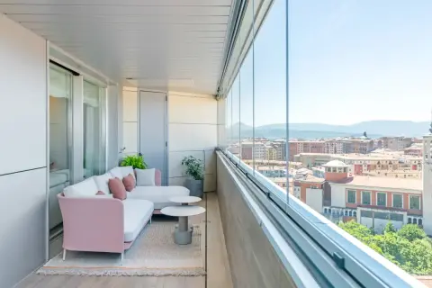 Sofá rosa y blanco en terrazas acristaladas con decoración moderna. Disfruta de la vista urbana desde este espacio acogedor.