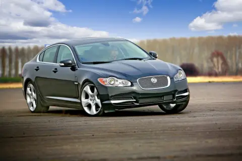 Czarny Jaguar XF na torze. Kierowca w środku, chmury na niebie. Wiele pozytywnych jaguar xf opinie potwierdza jego sportowy charakter.