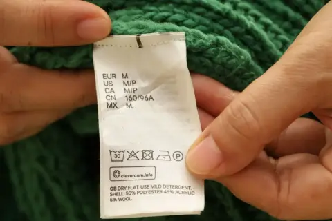 Etichetta di un maglione verde: non usare candeggina su poliestere. Asciugare in piano, usare un detergente delicato.