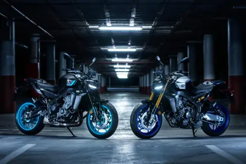 Dwa motocykle Yamaha MT, w tym jeden z niebieskimi felgami, prezentują swoją hyper naked estetykę w mrocznym garażu.