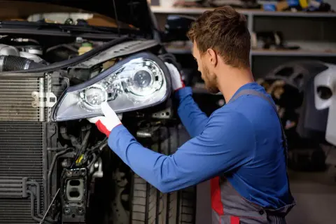 Mécanicien ajustant un phare sur une voiture, résolvant un feu en panne.