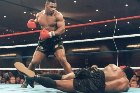 Mike Tyson står över en liggande motståndare i ringen. Hans imponerande fysik visar varför mike tyson vikt var så avgörande.
