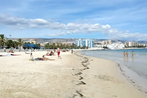 Spiaggia di Manfredonia con persone che prendono il sole e tre donne che camminano nell'acqua cristallina.