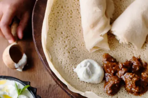 En hand tar en bit av en injera, en etiopisk rätt med kött och sås. Ett perfekt injera recept för en smakrik måltid.