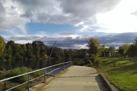 Paseo junto al río Miño, con el puente del Milenio y la playa fluvial de Ourense al fondo. Nubes amenazantes en el cielo.