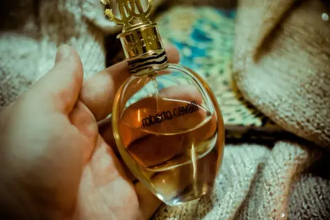Dłoń trzyma elegancką buteleczkę perfum Roberto Cavalli EDP z płynem w kolorze bursztynu, ozdobioną złotym korkiem i wzorem w panterkę.