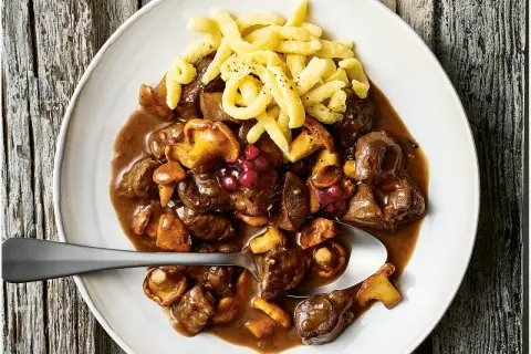 Herzhaftes Rehgulasch mit Rotwein, Pilzen und Preiselbeeren, serviert mit Spätzle. Ein köstliches rehgulasch rezept mit rotwein.