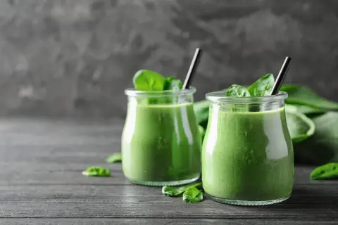 Dwa słoiczki pysznego, zielonego smoothie ze szpinakiem, udekorowane świeżymi liśćmi. Idealne na zdrowy początek dnia.
