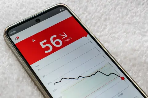 Niski poziom glukozy 56 mg/dL na ekranie telefonu, wskazujący na hipoglikemię reaktywną. Wykres pokazuje gwałtowny spadek.