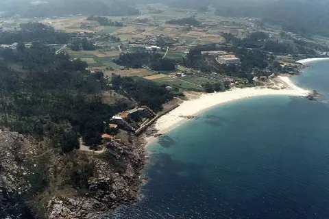 Vista aérea de la **playa de Cabeiro**, con arena blanca, aguas turquesas y un paisaje rural salpicado de casas y vegetación.