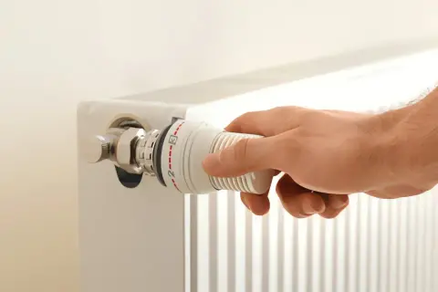 Hand dreht am Thermostatventil eines Heizkörpers. Die Markierungen zeigen eine Einstellung zwischen 2 und 3. Möglicherweise ist der Thermostat defekt.