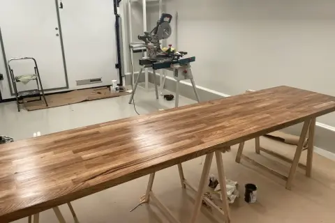 Långt ekbord på sågbockar, redo att behandla ekbordet. Kap- och geringssåg i bakgrunden.