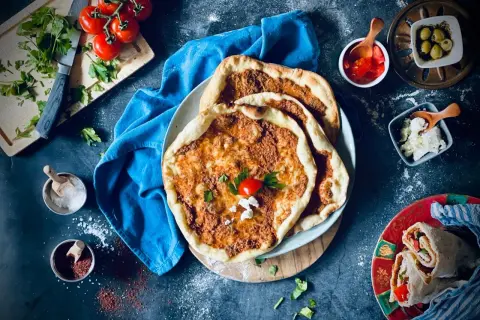 Lahmacun rezept original: Fladenbrot mit Hackfleisch, Tomaten, Petersilie und Käse, daneben Oliven und ein Wrap.